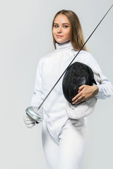 Young fencer athlete wearing fencing costume holding the sword and mask. Isolated on white...