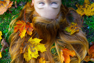 red haired girl laying in grass with golden autumn leaves on hair