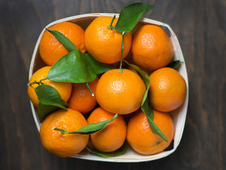 Mandarins with leaves in a wooden box on a wooden black background, top view