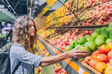 young adult woman choosing apples in grocery store