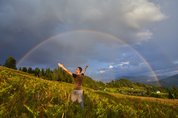 A happy man enjoys the rainbow in the mountains.