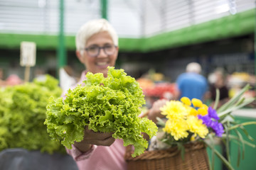Senior woman holds basket with flowers and  buys lettuce on market