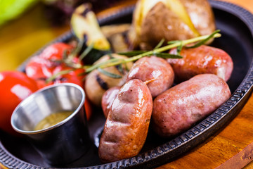 Sausages and grilled vegetables with sauce on black plate. Close up