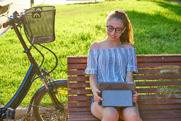 Girl sitting on park bench playing with tablet