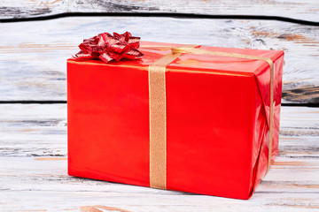 Red large Christmas gift box. Red box with present tied with golden ribbon on old wooden...