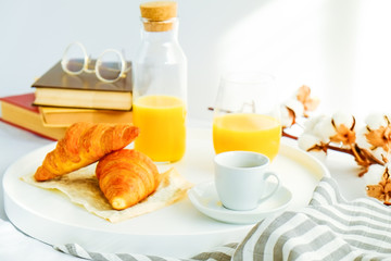 Morning breakfast in bed, white tray with glass of fresh orange juice, cup of coffee and french croissant, vintage eye glasses and books, stripped blankets. Close up, top view, background, copy space.