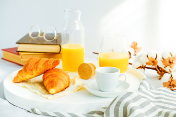 Morning breakfast in bed, white tray with glass of fresh orange juice, cup of coffee and french croissant, vintage eye glasses and books, stripped blankets. Close up, top view, background, copy space.