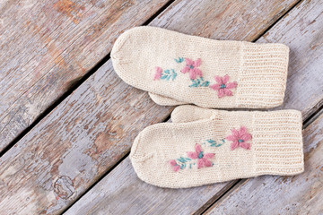 Pair of female warm woolen mittens. White embroidered knitted gloves for ladies on rustic wooden background. Beautiful handmade Christmas gift.
