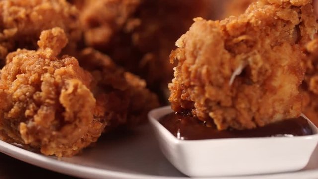 Hand put crispy fried chicken legs into barbecue sauce before eat.