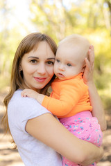 happy mother hug her baby daughter smiling in the green park near forest in sunlight outdoor shot