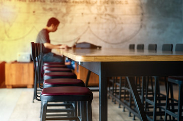 Vacancy chairs and wooden table with blurred unidentified man working with his laptop in background