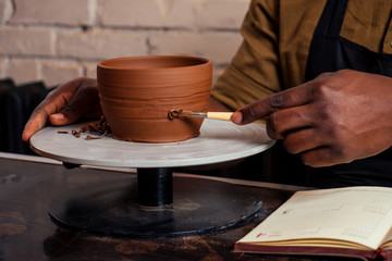 happy African American businessman potter male owner making clay sculpture pot cup vase at workbench in workshop studio . creativity and creative china shop merchant