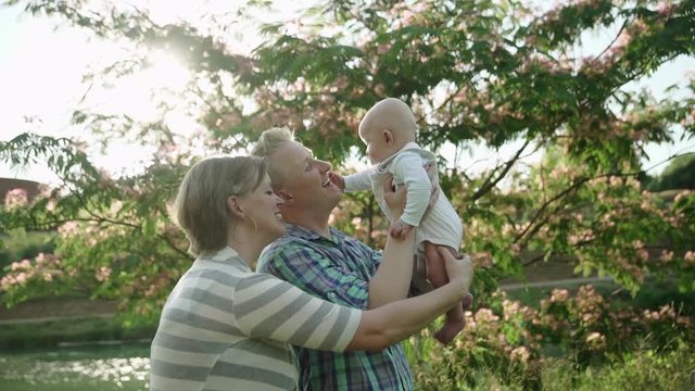 Happy parents play with the baby boy in their arms in summer park Slow motion Full HD