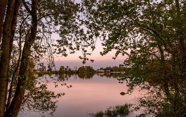 Obraz premium peaceful Fraser River framed by trees with sunset colors reflected in calm water in Ladner British Columbia 