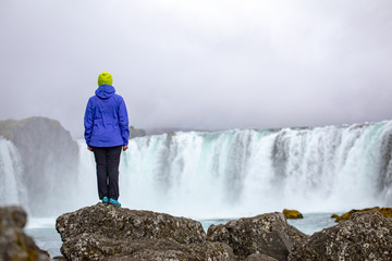 Obraz premium A beautiful young woman is standing against the backdrop of a beautiful waterfall. Iceland