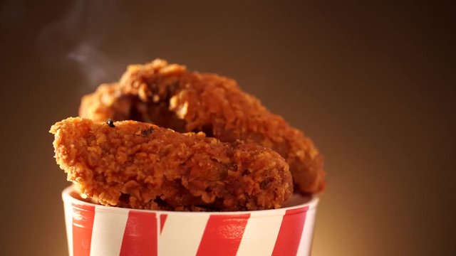 Rotation Bucket full of crispy kentucky fried chicken with smoke on brown background.