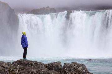Obraz premium A beautiful young woman is standing against the backdrop of a beautiful waterfall. Iceland