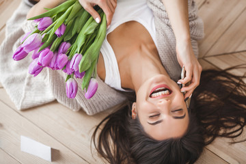 Cheerful young woman talking on the phone and holding flowers. Beautiful lady with tulips