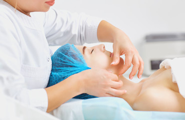 Beautician makes facial massage to a young woman in the spa salon.