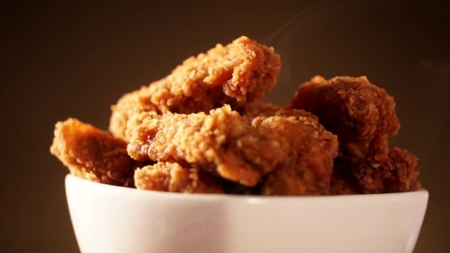 Rotation Bucket full of crispy kentucky fried chicken with smoke on brown background.