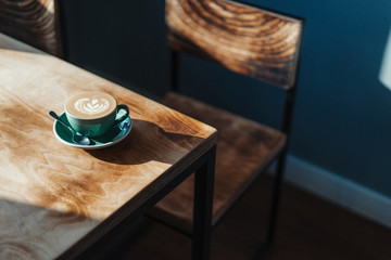 Close up of freshly brewed coffee cup on wooden table in modern bright cafe.