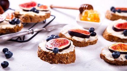 Sandwiches with creamy cheese. Ingredients: Blueberries, figs and Honey. Appetizer on a light background. Concept of a healthy breakfast.