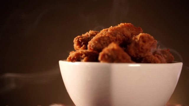 Rotation Bucket full of crispy kentucky fried chicken with smoke on brown background.