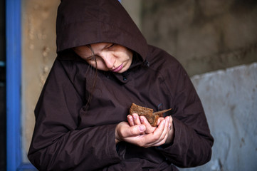girl in dark cape holds roll and black bread in her hands. woman rehearses role of beggar woman for  amateur performance.
