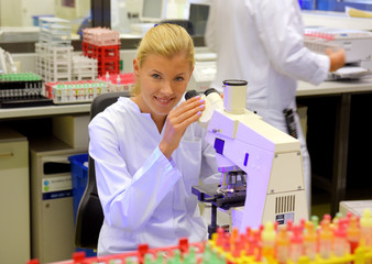 A young woman takes up her duties as  lab technitian. She wears a white smock to work with while...