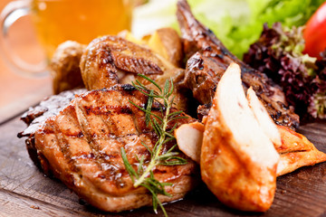 Mixed grilled meat and potato on wooden cutting board. Pork, beef, lamb, chicken, quail. Close up