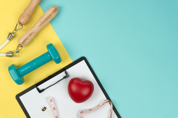 top view of the green dumbbell and jump rope, a red heart symbol and vinyl tape measure with black clipboard on the yellow and blue background