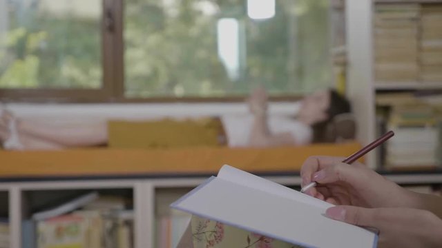 Hypnotherapy session with patient lying on sofa in private consulting room talking about her emotional issues while young psychoanalyst woman listening and taking notes