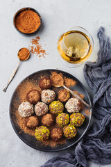 Variety of homemade dark chocolate truffles with cocoa powder, pistachios, almonds in light gray background texture. Top view, copy space.