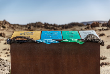 View of a large trash bin with compartments for different types of trash for recycling, in a desert...