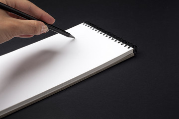 Human hand with pencil prepare to writing on notebook. Black background.