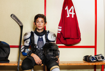 Naklejka premium Boy sitting on the bench in ice hockey locker room