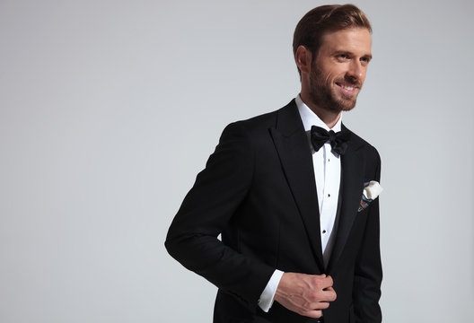 Young elegant man in tuxedo holding button and laughs