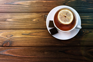 tea with lemon in a cup, two pieces of chocolate on a wooden background. dessert, tea, rest