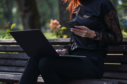 Woman using laptop and smartphone on bench