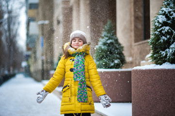 A little girl in a yellow jacket plays in the winter outside. The girl throws snow, sculpts snowy...