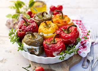 Roasted bell pepper with mushroom, rice, cheese and herbs filling in a baking dish on a white wooden table. A healthy and delicious vegetarian food.
