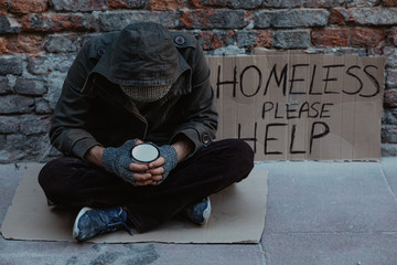 Homeless man sitting on the street in the shadow of the building and begging for help and money....