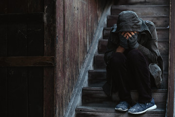 Homeless man sitting on the stairs of the old building andhe warms himself. Problems of big modern...