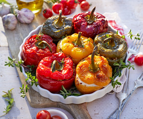 Roasted bell pepper with mushroom, rice, cheese and herbs filling in a baking dish on a white wooden table, close-up. A healthy and delicious vegetarian food.