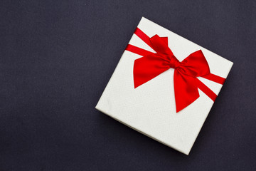 White gift box with red ribbon on black background. Top view.