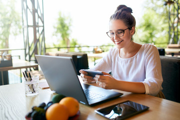 Handsome businessman distracted from work on the laptop watching video on smartphone. Freelancer...