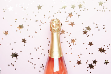 Christmas or New Year pink background with  bottle of sparkling wine, rose champagne and gold decor, top view