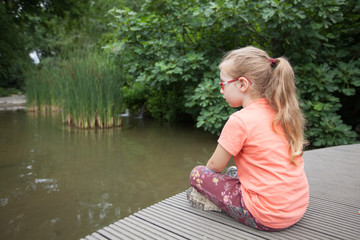 young girl sits on the bridge and looks at the pond