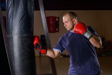 novice male boxer training with punching bag on dark background.