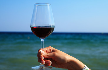 a young female is holding a red wine glass with sea background